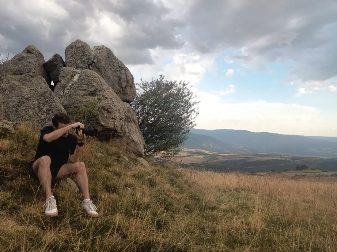Assis sur un rocher en montagne, l'appareil à l'œil, face à une vallée